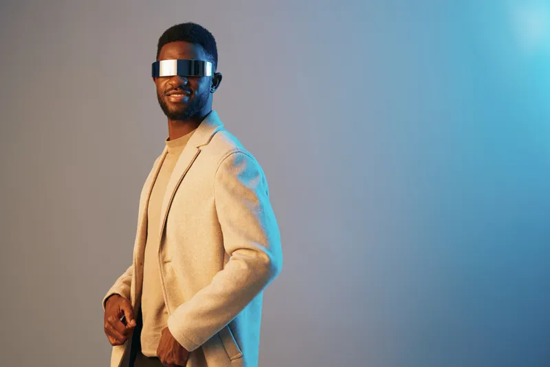 Stylish black man wearing futuristic sunglasses and a blazer, exuding confidence against a cool gradient background with blue tones