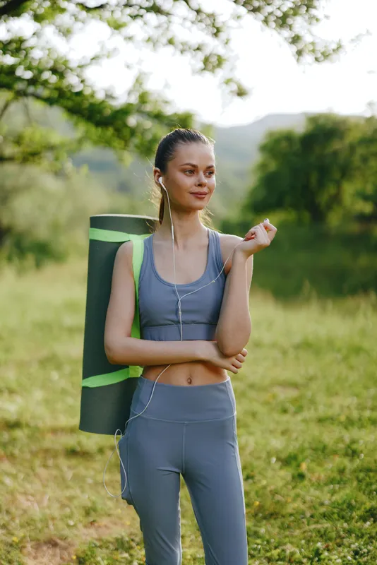 Young woman in activewear with yoga mat, enjoying nature, demonstrating healthy lifestyle and fitness concept in a serene outdoor setting