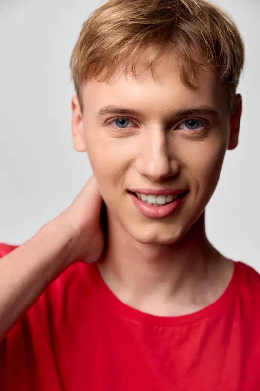 Smiling young man in a red shirt with hand on neck, close up, casual fashion mood, warm lighting and friendly expression suitable for lifestyle, branding, or model portfolio