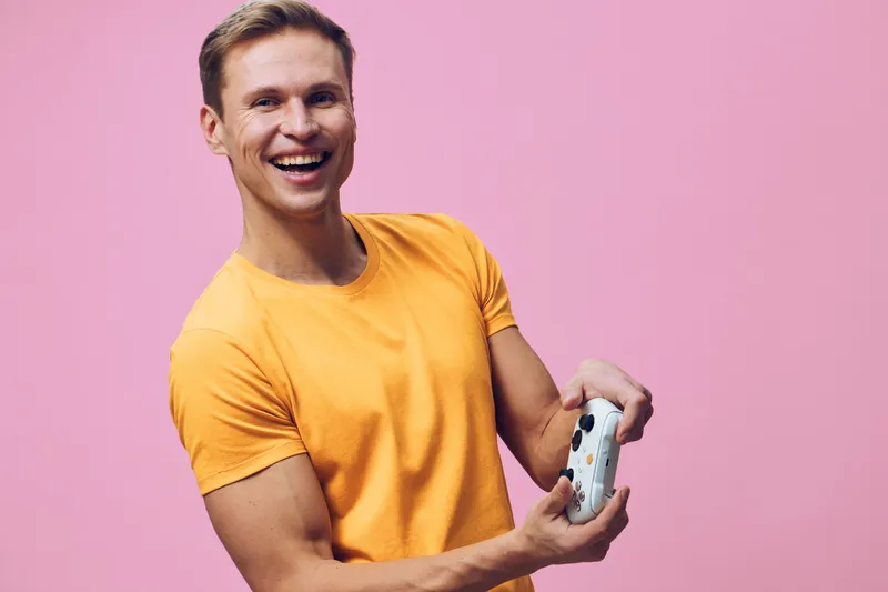 Smiling happy young caucasian man wear yellow t-shirt hold modern game controller isolated pink background cyber security concept digital lifestyle