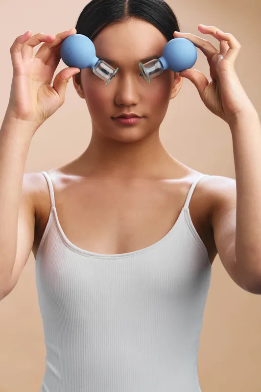 an asian woman is seen exercising in a clean studio, lifting small dumbbells near her eyes, focused and determined, conveying strength and wellness.