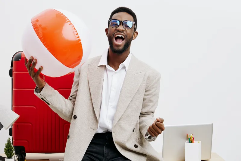 Smiling man with dark skin, sunglasses, beige blazer and white shirt holding a colorful beach ball, standing in bright studio with playful summer and vacation theme, vibrant colors, cheerful mood, lif