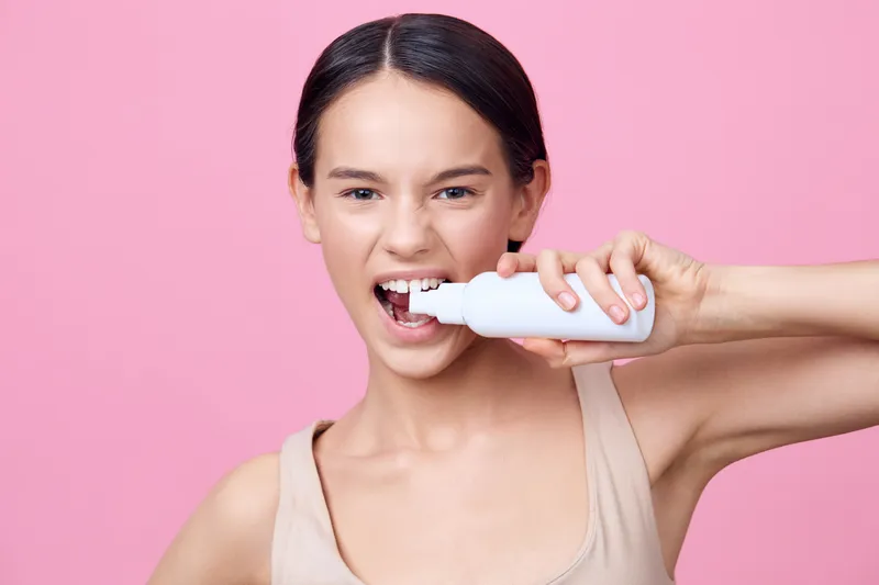 Young female model demonstrating a teeth whitening product on a pink background, expressing excitement Skincare, beauty, and dental health concept