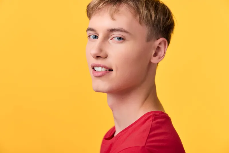 Closeup of a young man with a warm smile against a bright yellow background, wearing a red shirt, studio lighting, casual fashion, clean composition and upbeat mood.
