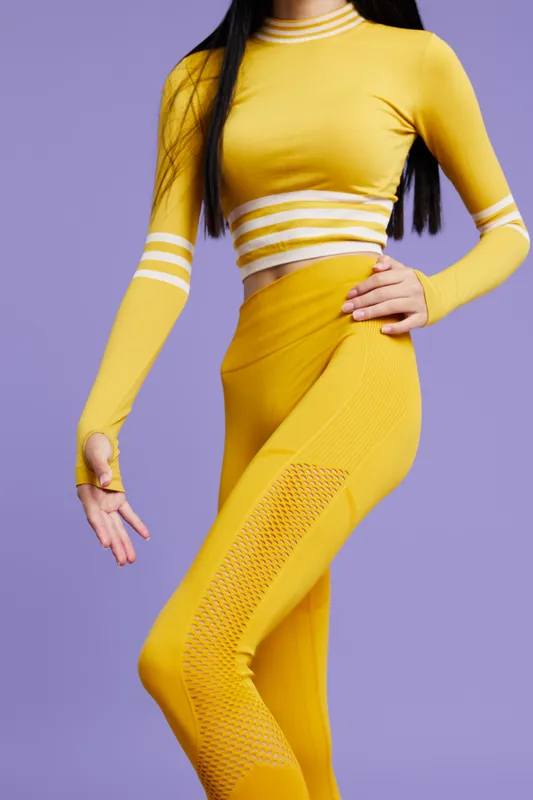 Sport fitness woman wearing bright yellow athletic outfit poses against purple background showcasing modern activewear and healthy lifestyle, focusing on movement and style.