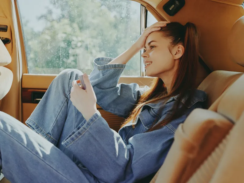 A young woman enjoying a moment of relaxation in a vintage car, dressed in denim, with a playful expression, capturing the essence of freedom and nostalgia.