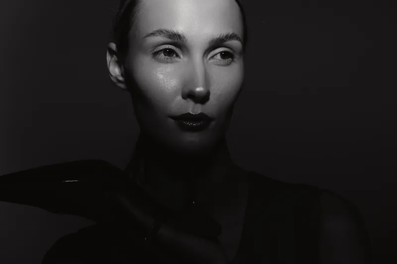 Close-up portrait of a white woman with pale skin in dramatic black and white lighting, creating a mysterious and elegant mood with strong shadows and highlights.