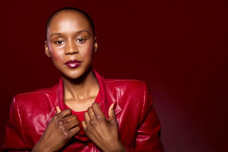 Confident black woman with dark skin wearing a red leather jacket poses against a red background. Studio portrait of a stylish African American female with short hair and bold makeup.