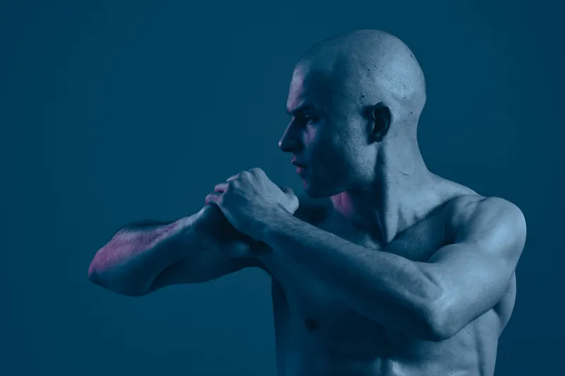 Athletic man with a focused expression showcasing strength and determination against a muted background. This image highlights the power of the human body in blue tones.