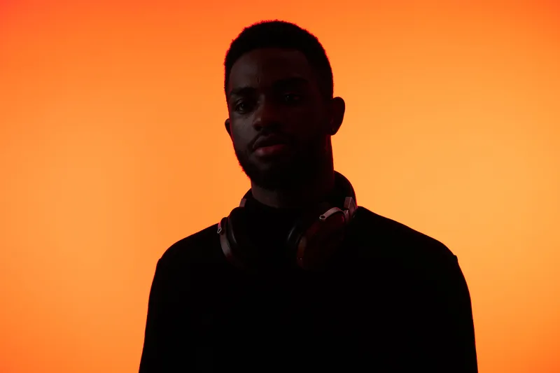 Dark silhouette of a young Black man with headphones against a vibrant orange background, embodying a modern and stylish concept of music and youth culture