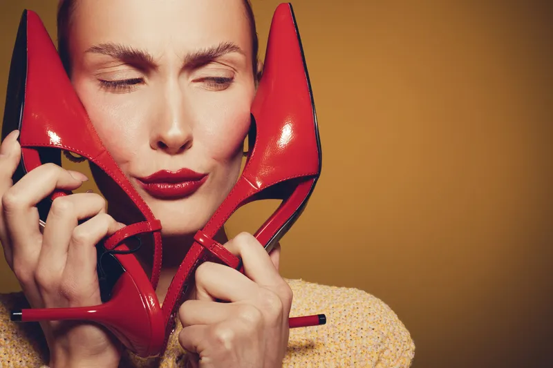 Woman with closed eyes holds red high heel shoes close to her face, expressing affection and style. Concept of fashion, beauty, footwear, and personal expression in studio lighting.