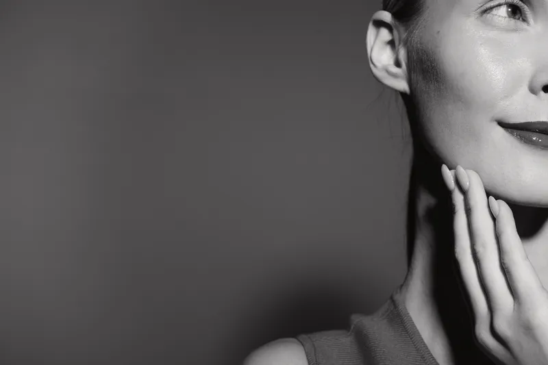 Close-up of a young Asian woman with smooth skin touching her face gently. Black and white portrait with soft lighting, concept of skincare and natural beauty.