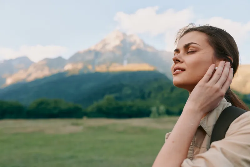 Woman outdoors enjoying fresh air and sunlight in a natural landscape, showcasing lifestyle, wellness, and self care. Soft light and open scenery create a peaceful mood.