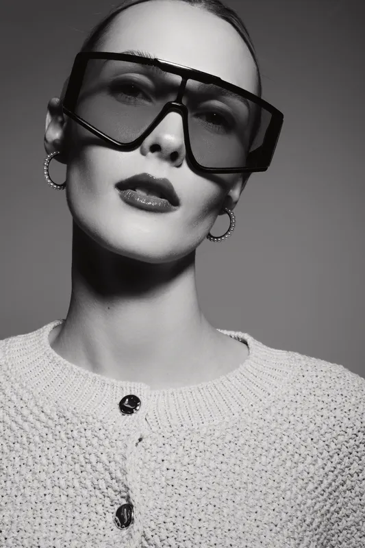 Close-up portrait of a white woman with pale skin wearing oversized sunglasses and hoop earrings. Fashion concept with monochrome studio lighting and stylish clothes.