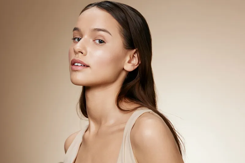 Beautiful young woman with long hair displaying natural beauty, soft expression, neutral background, perfect for promoting skincare or cosmetic products