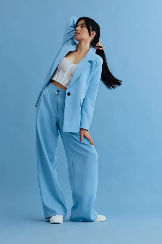 woman posing in blue suit with white lace top, long dark hair, light blue studio background, stylish casual fashion, modern outfit combination