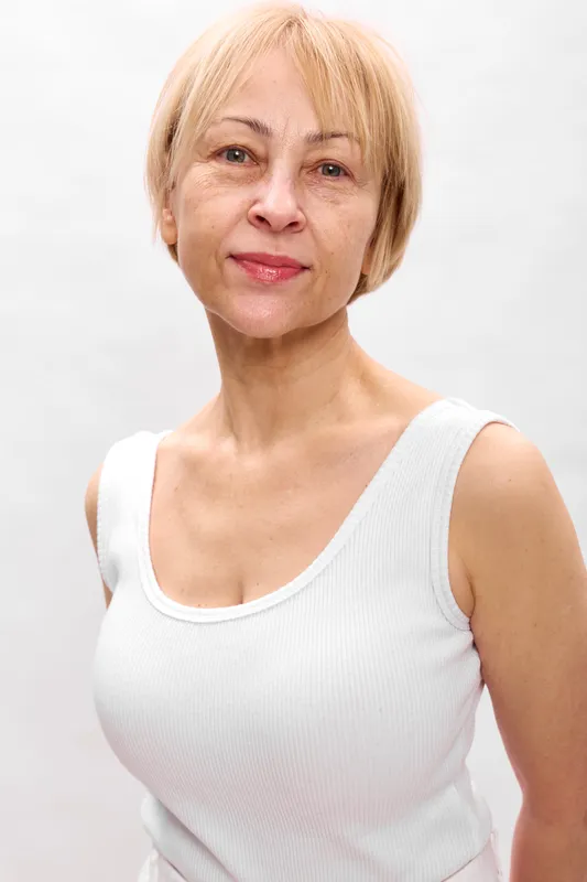 Woman portrait blonde mature smile white sleeveless studio closeup face, gentle expression in clean studio background, concept of calm beauty and confidence for adult wellbeing