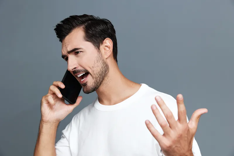 Expressive man talking on mobile phone, gesturing passionately while communicating. Modern lifestyle portrayed against a solid gray background, capturing enthusiasm.