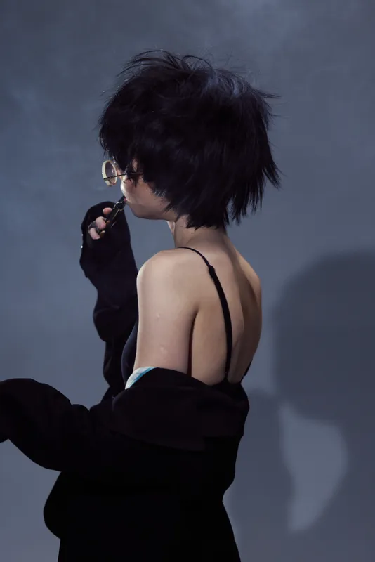 Stylish woman with short black hair wearing glasses and dark clothing in a moody studio setting