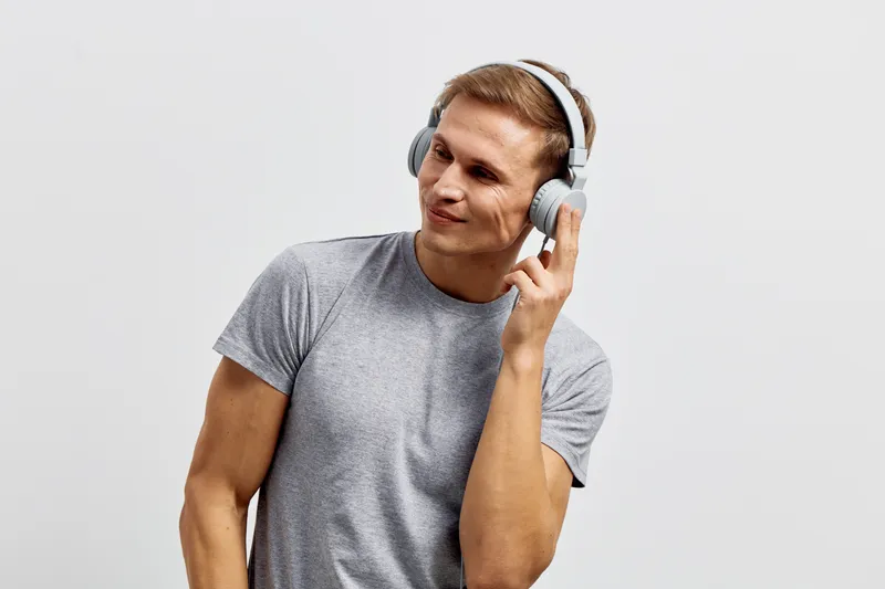 Smiling young caucasian man wear grey t-shirt listen music with wireless headphones isolated on light neutral background casual lifestyle concept