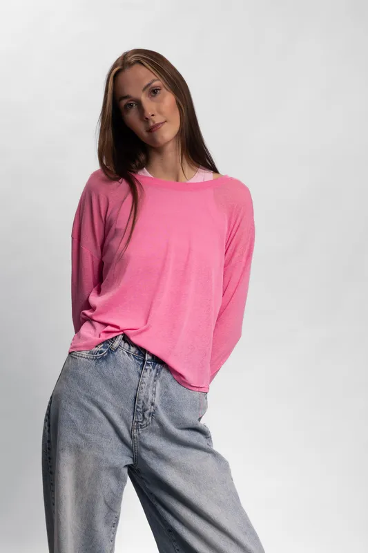 Young woman in pink sweater and loose jeans poses against a plain background. Casual fashion style with natural makeup and relaxed confident expression.