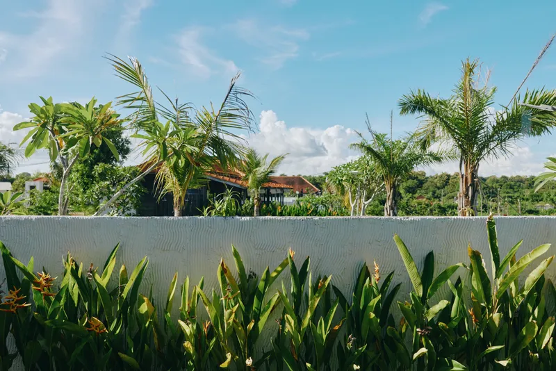 Cheerful outdoor scene with lush greenery, tropical plants, and a relaxed figure enjoying warm sunlight, a gentle breeze, clear blue sky, and tranquil garden vibes and relaxed posture.