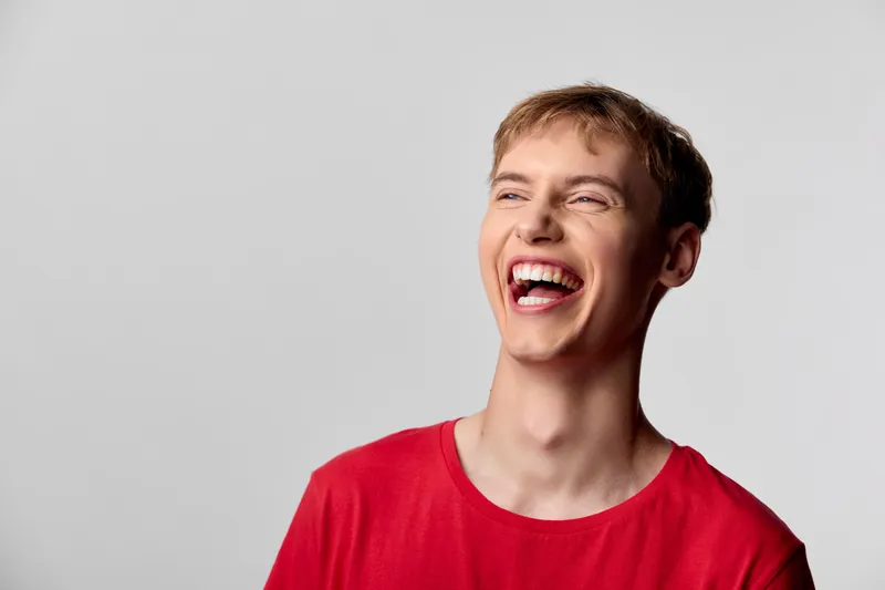 Laughter, man in a red t shirt, captured in a bright studio setting, exudes spontaneous joy, upbeat energy, and positive mood ideal for lifestyle, happiness, and social media campaigns
