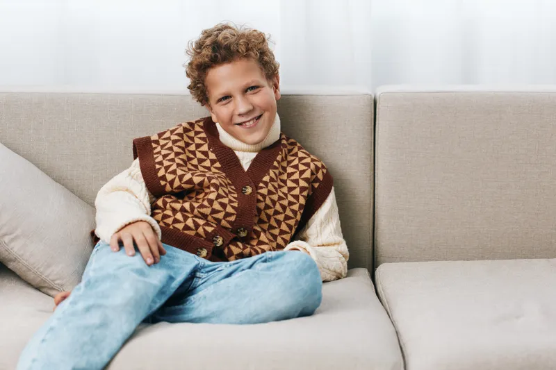 Authentic image of a cheerful child on a sofa, highlighting a playful school theme and a relaxed lifestyle through warm light, cozy attire, and a candid, homey moment.
