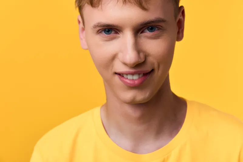 Young man in a yellow shirt against a bright yellow backdrop, smiling softly in a clean studio shot, simple fashion vibe, cheerful mood, close crop highlighting facial features