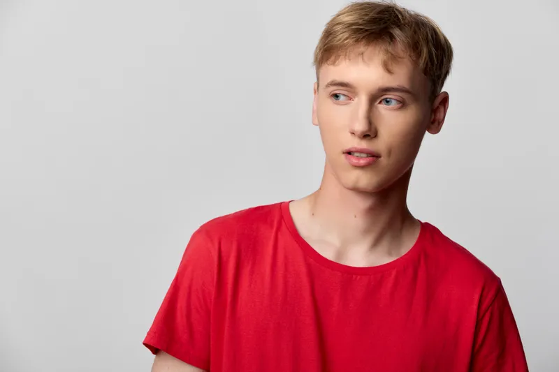 Man wearing a red shirt in a studio setting, looking to the side with a thoughtful expression, casual mood and clean background for lifestyle, fashion, or advertising use