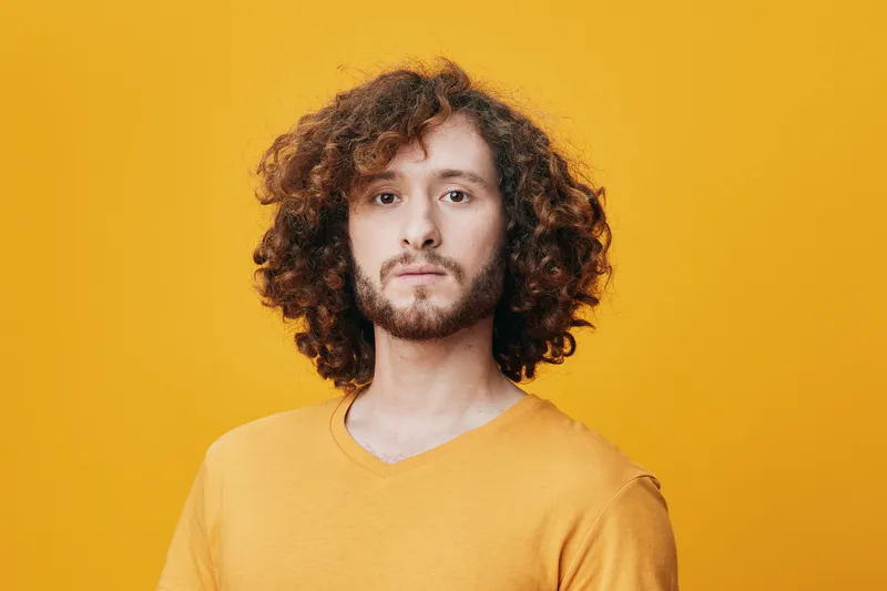 Young man with curly hair wearing a yellow t shirt against a vibrant yellow background, exuding confidence and creativity, ideal for lifestyle and fashion themes