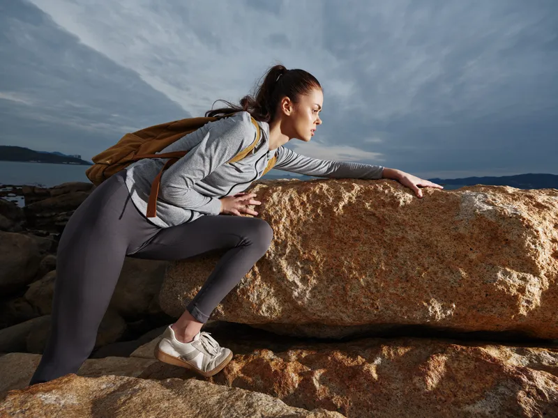 Young athletic woman climbing a rock during an outdoor adventure, showcasing determination and strength against a dramatic sky background