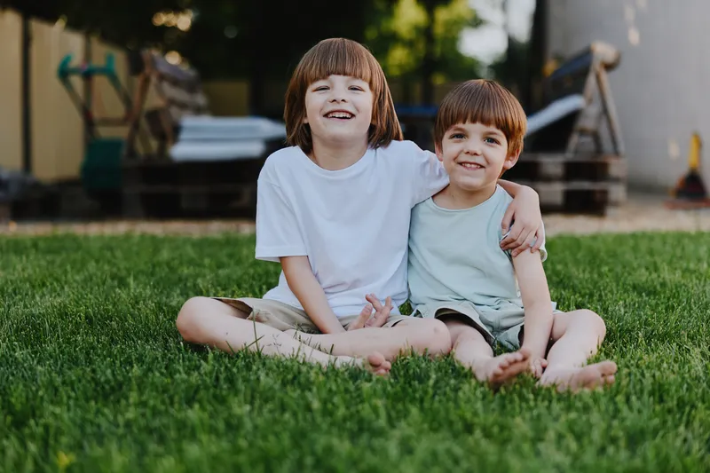 Smiling boys enjoying a sunny day, sharing a moment of friendship on a grassy lawn, radiating joy and innocence in a relaxed outdoor setting.