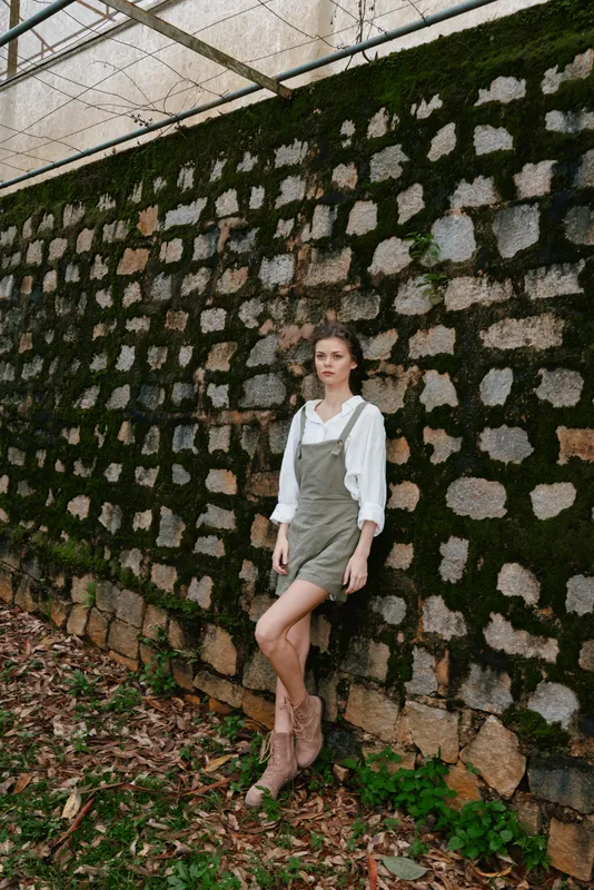 Young woman in a green dress stands confidently against a stone wall, showcasing a blend of elegance and nature, ideal for seasonal fashion and lifestyle concepts