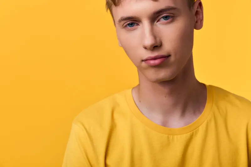 Close up of a young man wearing a yellow t shirt against a solid yellow background, calm expression, studio shot, warm color palette for fashion and lifestyle branding