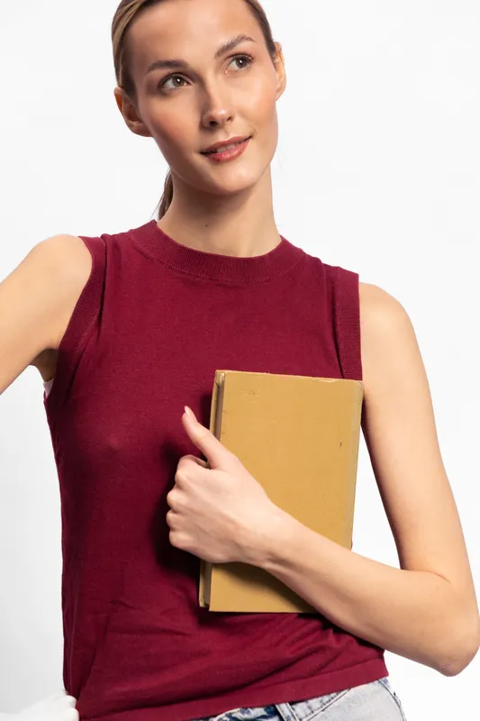 Young woman in sleeveless red top holds a closed book close to chest, looking away thoughtfully. Concept for education, knowledge, and casual lifestyle.