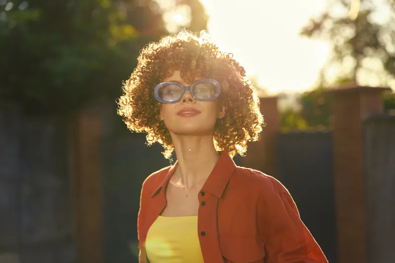 Vibrant woman lifestyle outdoors sunny portrait, confident and casual in a yellow top and jacket. Natural light enhances warmth and glow, capturing urban vibe and fashion theme