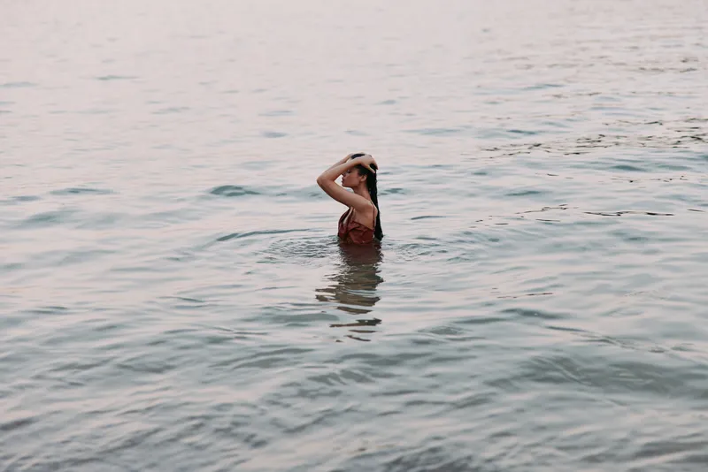 Woman relaxing in water during sunset with calm sea and soft light, enjoying peaceful moment and summer vibe near the beach shore.