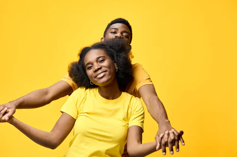 Cheerful couple holding hands on a bright yellow background, showcasing joy and connection in matching yellow shirts, perfect for romantic or friendship themes