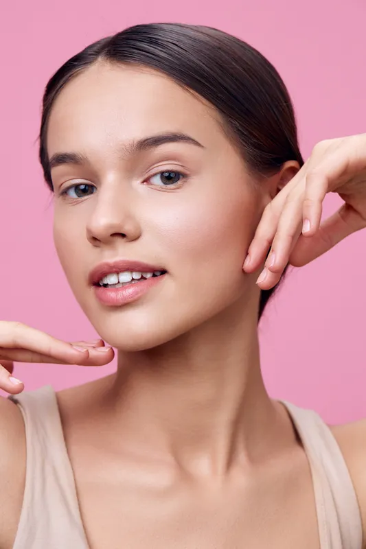 Young woman with natural makeup and a soft smile posing against a pink background, showcasing beauty and confidence Perfect for beauty and skincare themes