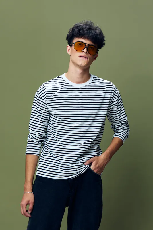 Young man wearing striped shirt and sunglasses posing confidently against green background, casual style and modern urban fashion vibe.