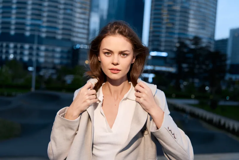 Confident business woman in stylish outfit outdoors with urban background, showcasing professional elegance and determination in modern environment.
