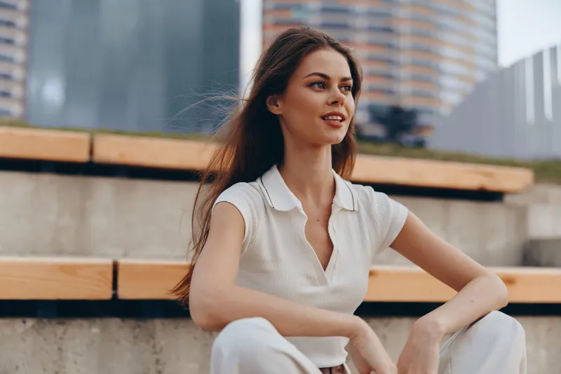 Businesswoman outdoors in modern setting, exuding confidence and style, dressed in casual chic attire with natural makeup, showcasing a professional yet approachable demeanor.