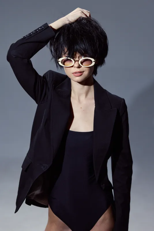 stylish woman wearing black blazer and sunglasses posing with hand in hair in studio lighting