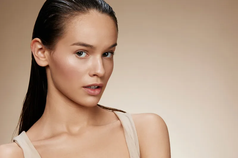 Close up portrait of a serene young model with wet hair, conveying confidence and beauty against a warm beige background, highlighting natural skin tones and features