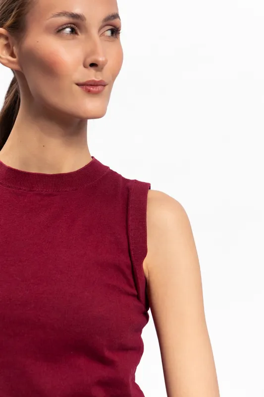 Young woman in sleeveless red top looks to the side with a subtle smile. Studio portrait on white background with natural makeup and soft lighting, concept of casual fashion and confidence.