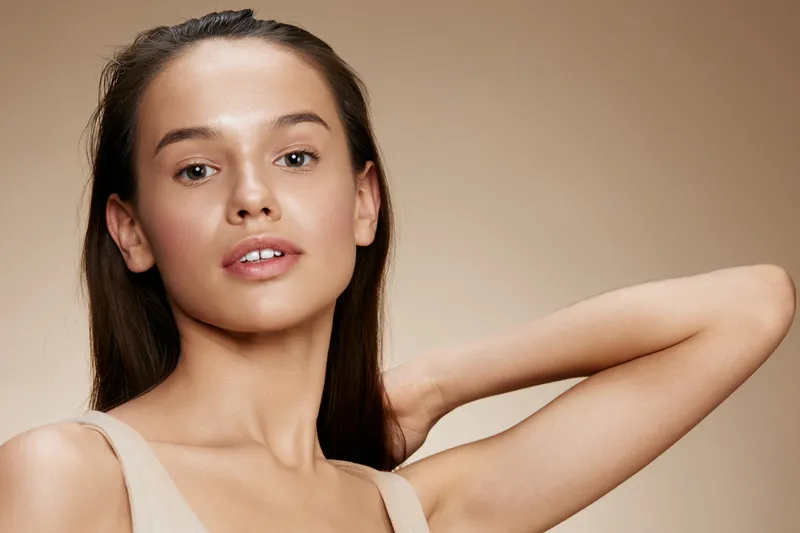 Natural beauty portrait of a young woman showcasing flawless skin and subtle makeup against a neutral background, highlighting skincare and self care concepts