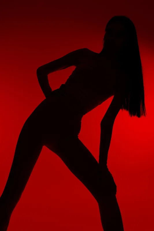 Silhouette of a woman sport fitness posed against a striking red background, showcasing active and dynamic body posture in minimal athletic wear, emphasizing strength and movement.