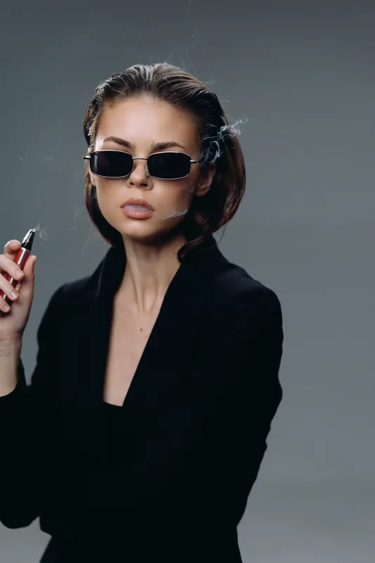 Stylish woman wearing sunglasses and black blazer holding a cigarette with a serious expression