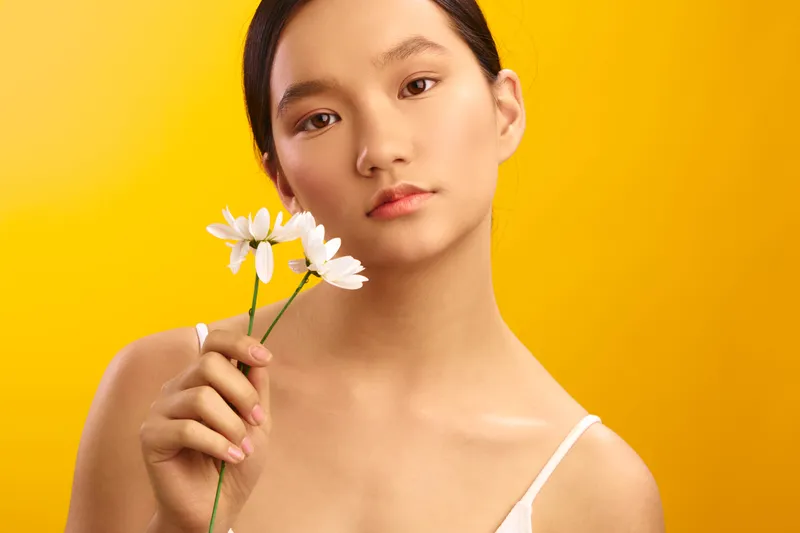 asian woman holds white flowers against a vibrant yellow background, creating a clean and minimalist portrait with calm mood, soft light, and subtle elegance.
